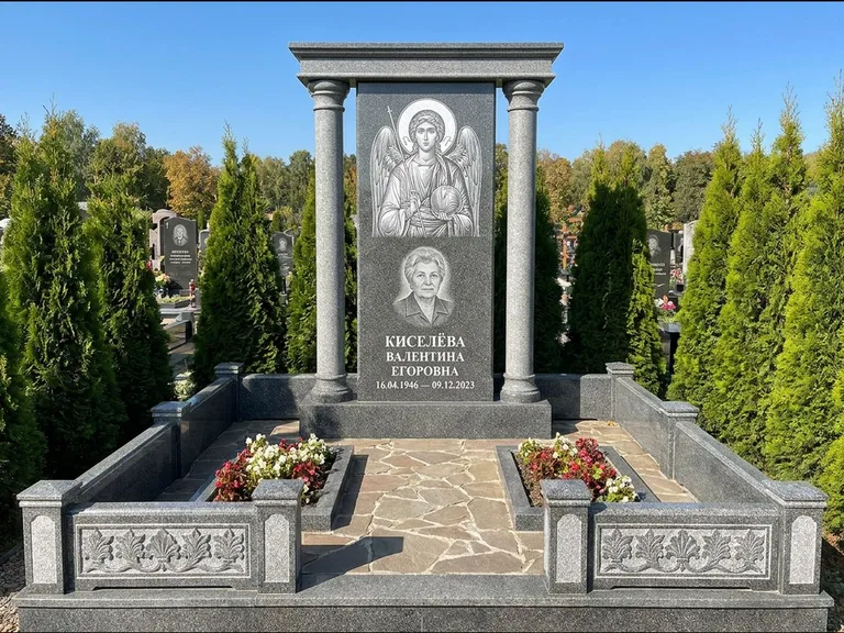 Памятник с гравировкой иконы: массивная стела с двускатным навершием-домиком — гравировка Николая Чудотворца, живая изгородь из туи, работа «Журавлёв» в Новосибирске
