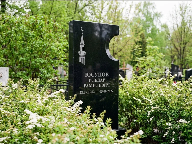 Мусульманский памятник с гравировкой мечети: стела с боковым вырезом в форме полумесяца — гравировка минарета с полумесяцем, низкие кусты спиреи в цвету, работа «Юсупов» в Новосибирске